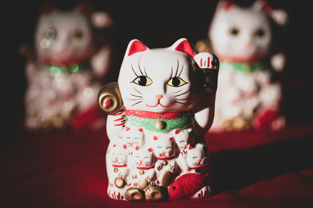 A white and red ceramic maneki-neko figurine with one paw raised