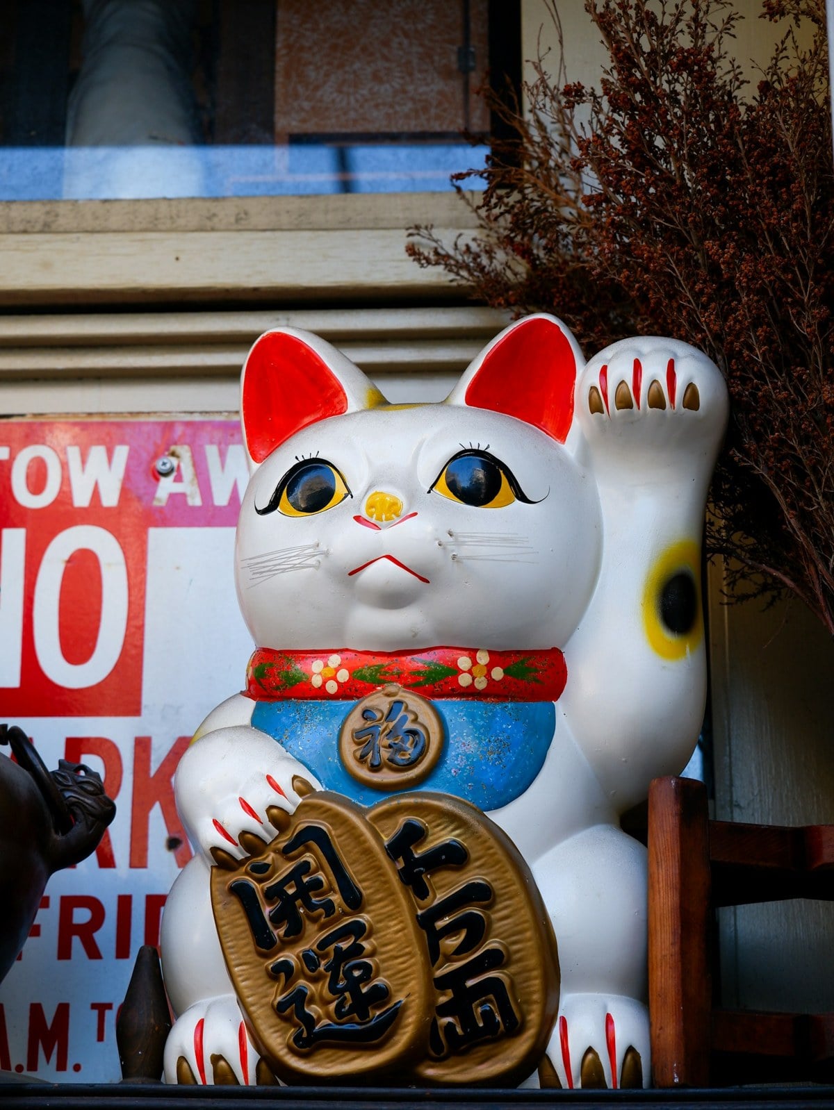 A white maneki-neko statue with one raised paw in a shop window
