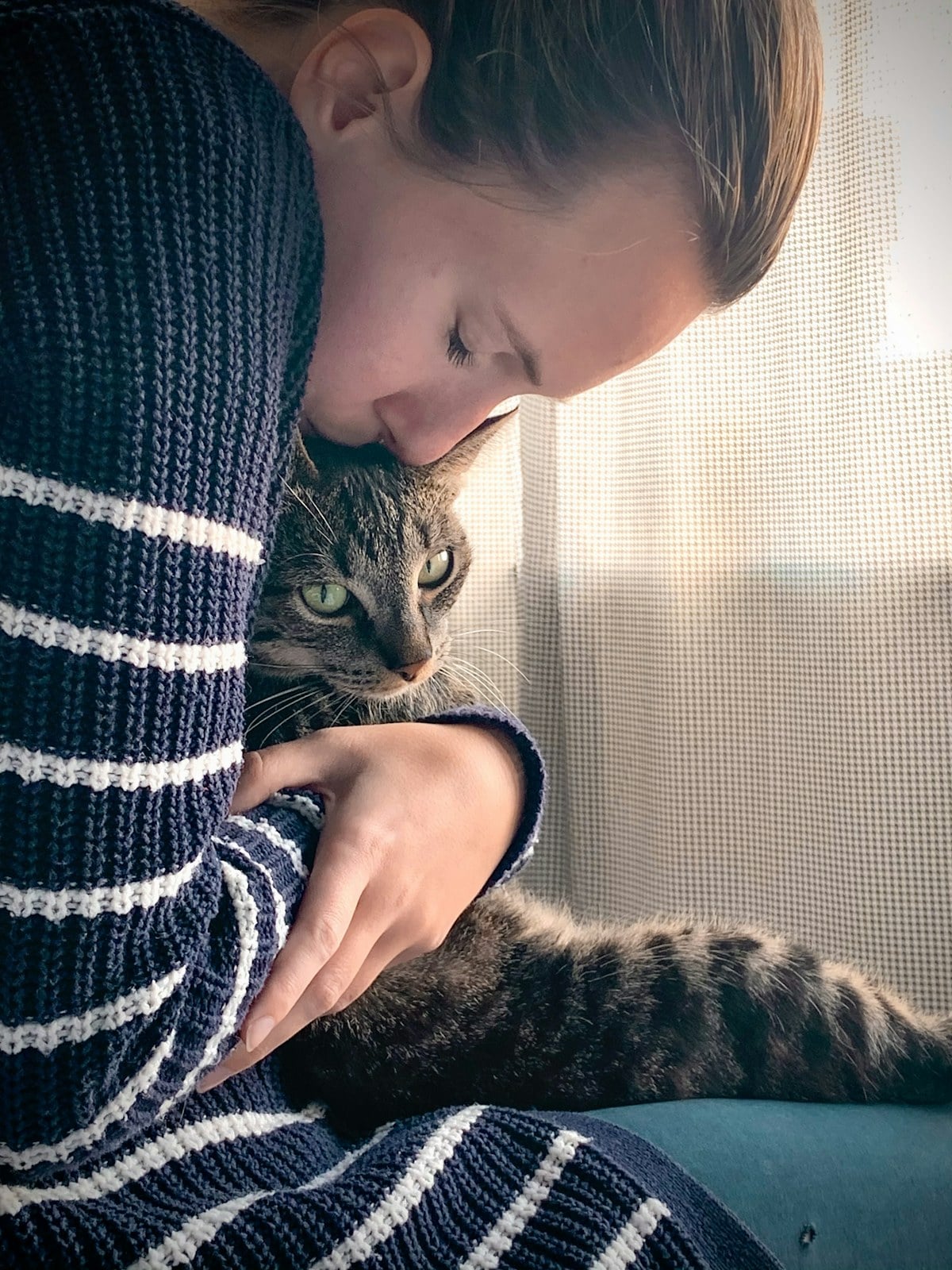 A woman holding a tabby cat close, cheek against its head